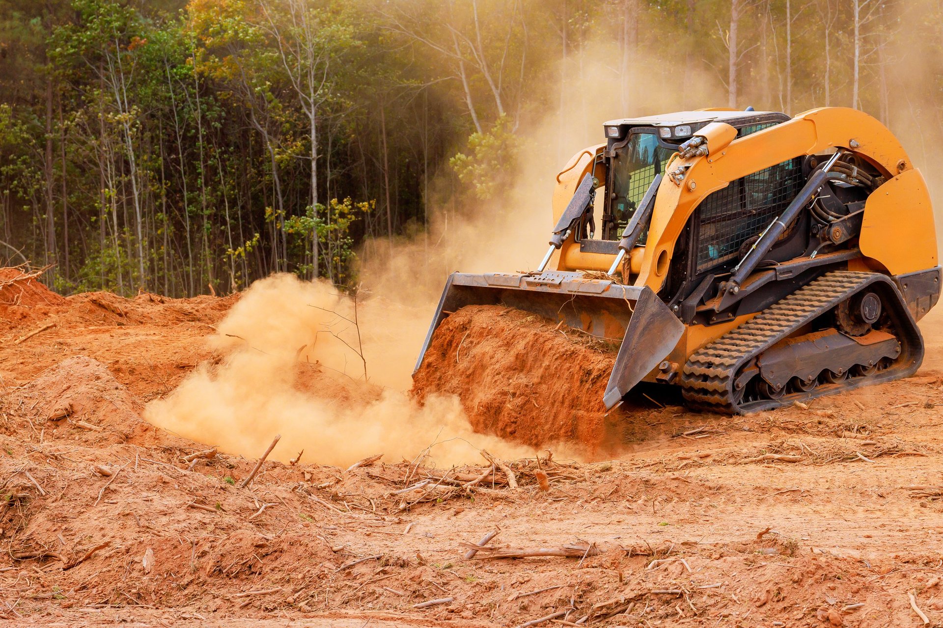 Heavy machinery clears land covered in dust among trees, preparing site for future development activities