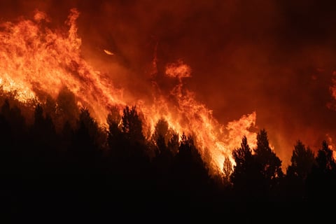 Wildfire burning across dry forested hillside with thick smoke rising into the sky
