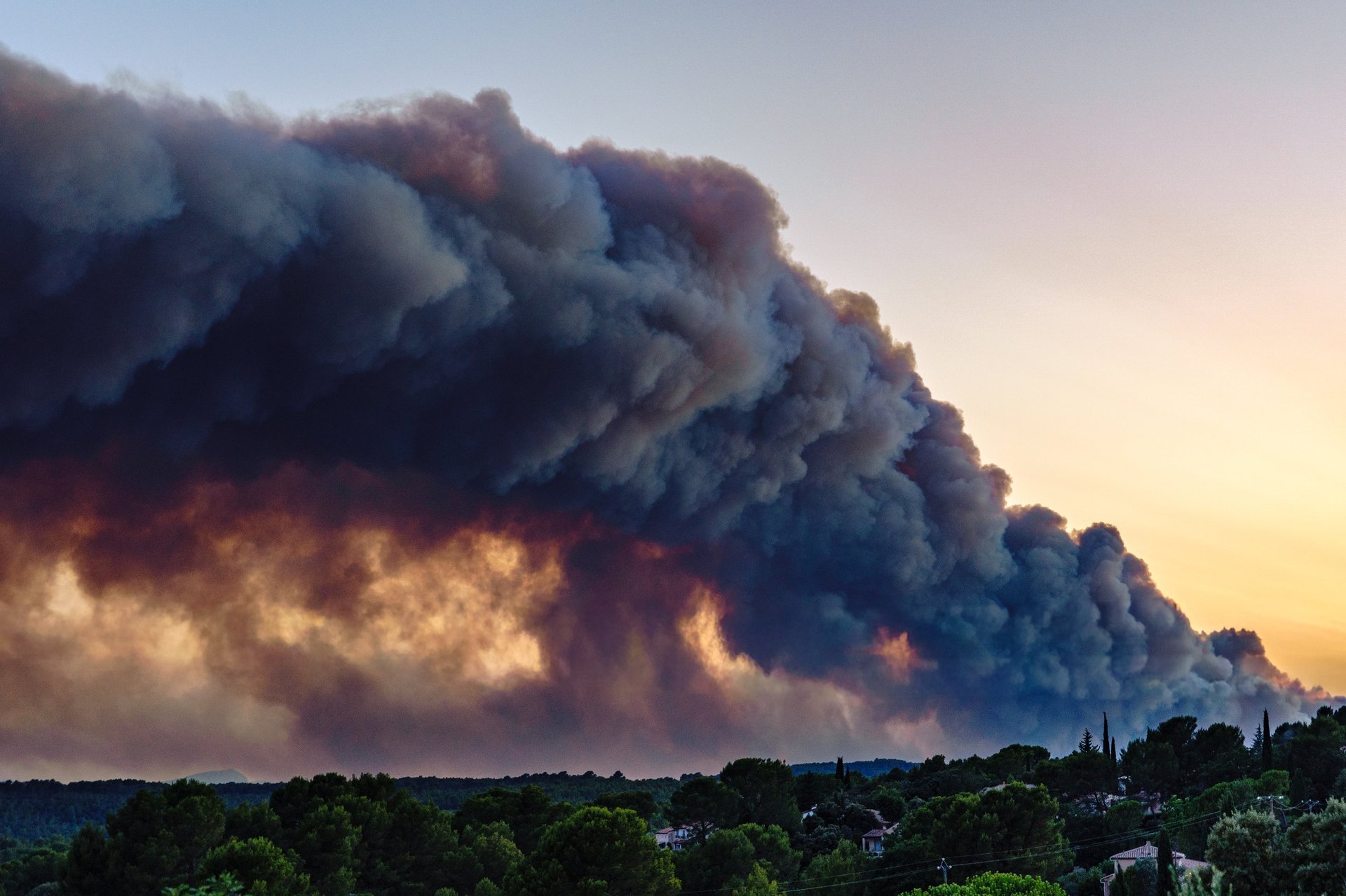 Dramatic plume of smoke rising above forested hills during a wildfire