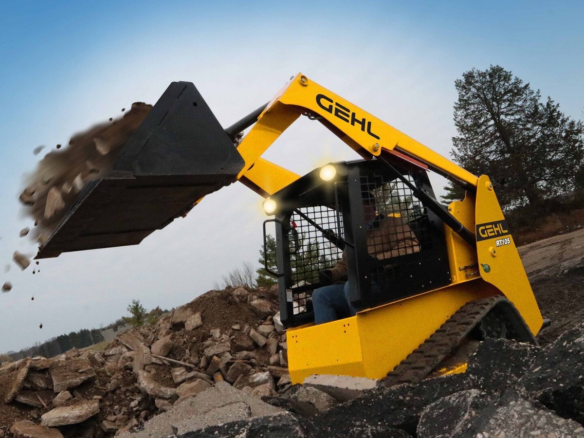 Yellow Gehl compact track loader with bucket raised, dumping dirt and rocks at a construction site
